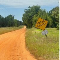 photo of dirt road in rural setting with "loose gravel" sign