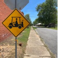 Street and sidewalk in small rural town with road sign for "golf cart" crossing