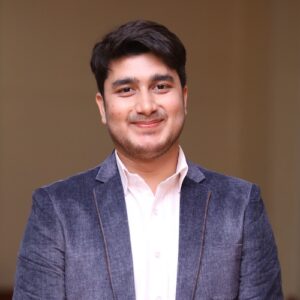 Man smiles for a headshot in a white shirt and navy jacket