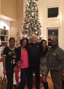 A group of people smiles in front of a Christmas tree.